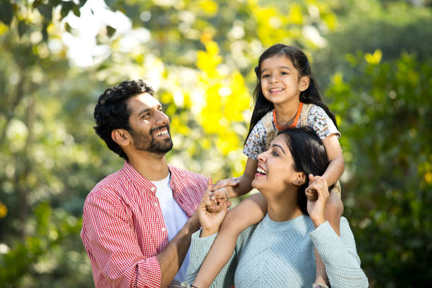 Happy mother with father carrying their daughter on shoulder at park
